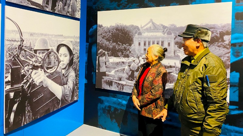 Bà Đặng Thị Ty cùng chồng ngắm bức ảnh của chính mình khi đang chiến đấu năm xưa. (Ảnh NVCC)