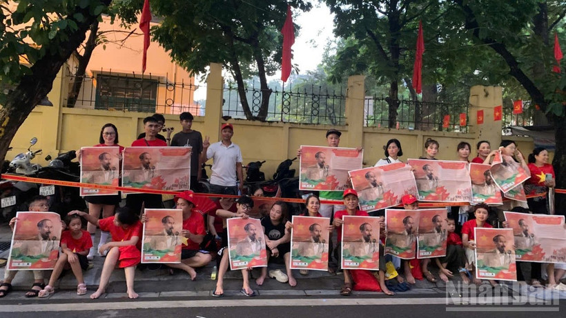 Người dân giơ cao tờ phụ san Báo Nhân Dân in ảnh Bác Hồ chào đón đoàn xe diễu binh trên đường Cửa Bắc.