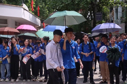 Tình nguyện viên hỗ trợ che ô cho thí sinh sau khi hoàn thành bài thi.