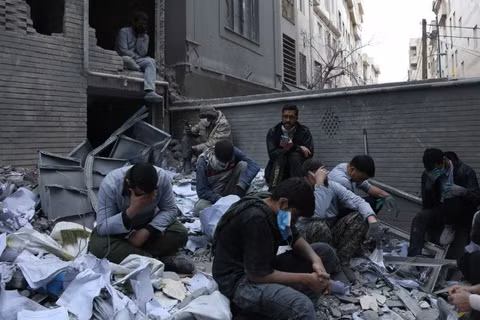 Người dân Iran bên những toà nhà đổ nát sau các cuộc không kích của Mỹ và Israel xuống thủ đô Tehran ngày 15/3/2026. (Ảnh: THX/TTXVN)