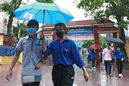 Các tình nguyện viên áo xanh che ô đưa từng thí sinh vào phòng thi tại điểm thi Trường Trung học phổ thông Nguyễn Khuyến (thành phố Nam Định).