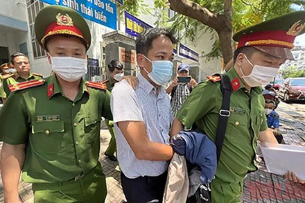 Cảnh sát áp giải ông Trần Quốc Huy, Trưởng Phòng Tổ chức-Hành chính CDC Khánh Hòa rời khỏi trụ sở làm việc. (Ảnh: THÀNH LONG)