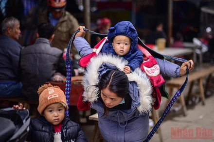 Khoảnh khắc người mẹ trẻ dân tộc H’ Mông quấn dây buộc địu con trên lưng tựa như cánh chim tung cánh che chở cho con. (Ảnh: Thành Đạt) 