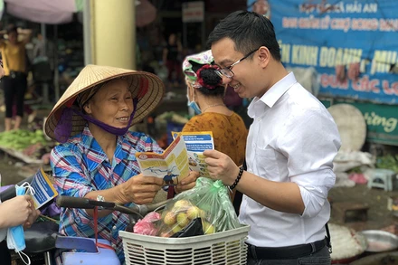 Người dân được phát tờ rơi và tư vấn về chính sách BHXH, BHYT. Ảnh: TÂM TRUNG.