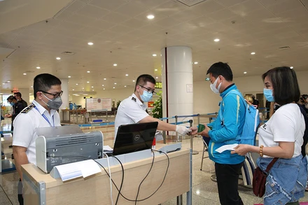 Nhân viên y tế kiểm tra phiếu khai báo y tế của hành khách trước khi làm thủ tục nhập cảnh tại cửa khẩu Sân bay quốc tế Nội Bài (Ảnh: TTXVN)