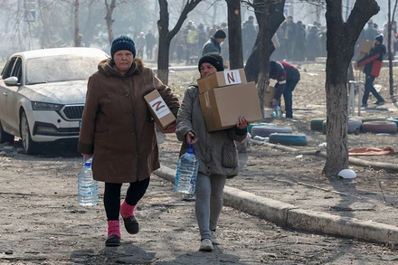 Người dân địa phương mang hàng viện trợ nhân đạo do binh sĩ Nga phân phát tại khu vực cảng Mariupol, Ukraine, ngày 23/3. (Ảnh: Reuters)