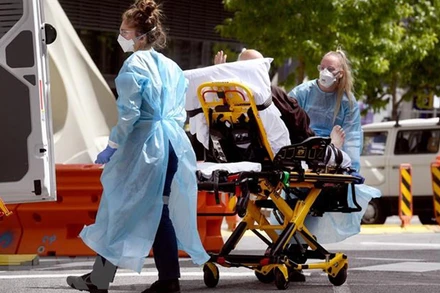 Nhân viên y tế chuyển bệnh nhân Covid-19 tới bệnh viện tại Melbourne, Australia. (Ảnh: AFP/TTXVN)