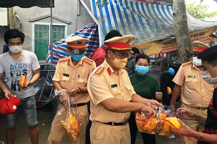 Lực lượng công an phát bánh mì, nước uống cho bà con trong lúc chờ xe đến đón về địa phương cách ly theo quy định.