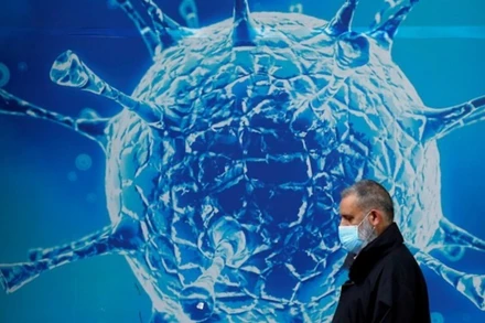 Người dân đeo khẩu trang đi ngang qua hình ảnh minh họa cho virus SARS-CoV-2. (Ảnh: Reuters)