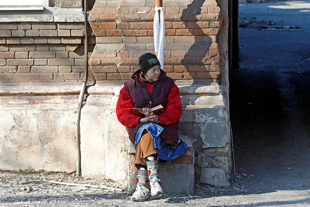 Người dân ngồi bên nhà một ngôi nhà bị hư hại do chiến sự tại Mariupol, Ukraine, ngày 7/4. (Ảnh: Reuters)