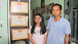 Em Phạm Thị Hậu và cậu ruột Ngô Thanh Đoàn đứng bên các thành tích học của em Hậu.