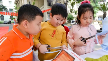 Các học sinh Trường tiểu học Tràng An cắt dán mô hình Cột cờ Hà Nội tại triển lãm của Báo Nhân Dân. (Ảnh THẾ ĐẠI)