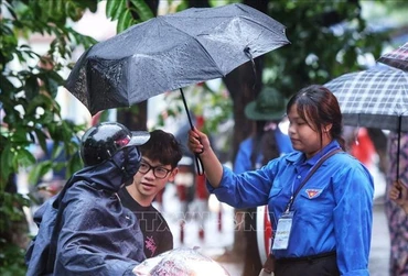 Tình nguyện viên hỗ trợ đón thí sinh vào điểm thi trong cơn mưa sáng 9/1 (Ảnh: TUẤN ANH/TTXVN)