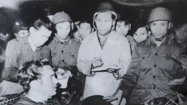 Nhà báo Phạm Thanh (người mặc áo khoác trắng) cùng nhà báo Đỗ Quảng (người đầu tiên, bên trái), phỏng vấn phi công lái máy bay B52 Mỹ bị bắt tại bãi đá Phương Liệt, Hà Nội đêm 25/12/1972. Ảnh: Bảo tàng Báo chí Việt Nam