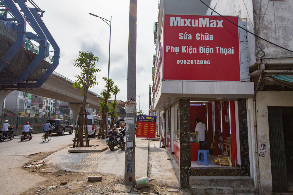 Cửa hàng phụ kiện điện thoại của anh Thế Thành nằm trên mặt đường Minh Khai. Do giải phóng mặt bằng nên hiện chưa có địa chỉ, số nhà cụ thể. Anh Thành mới kinh doanh được 4 tháng, lúc thuê thì mặt bằng đã nhỏ như hiện tại, rộng 2m, mặt tiền gần 8m. Nhà siêu mỏng trên đường vành đai 2 -0