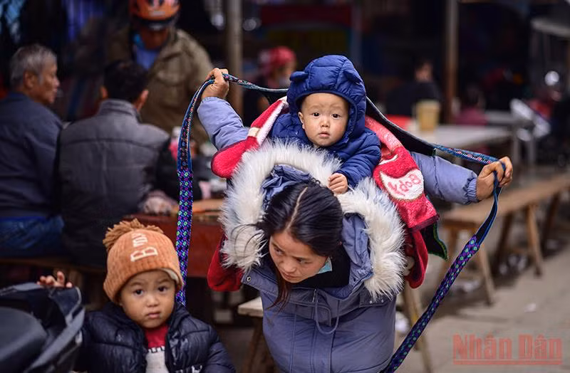 Khoảnh khắc người mẹ trẻ dân tộc H’ Mông quấn dây buộc địu con trên lưng tựa như cánh chim tung cánh che chở cho con. (Ảnh: Thành Đạt) 