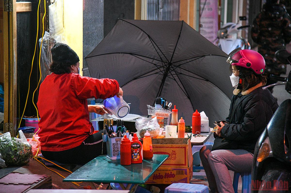 Chị bán hàng ăn ngoài vỉa hè thì căng tam cái ô lên để tránh gió rét. (Ảnh: THÀNH ĐẠT) Hà Nội: Người lao động và người vô gia cư căng mình chống chọi với giá rét -0
