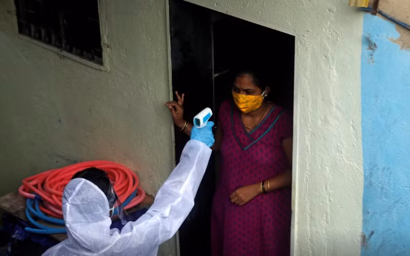 Nhân viên y tế đo thân nhiệt của người dân sống trong khu ổ chuột tại Mumbai, Ấn Độ, ngày 27-6. (Ảnh: Reuters)