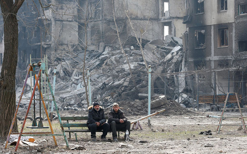 Người dân địa phương ngồi gần một tòa chung cư tại TP Mariupol, Ukraine, ngày 25/3. (Ảnh: Reuters)