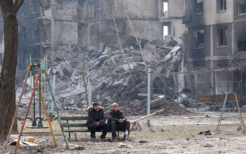 Người dân địa phương ngồi gần một tòa chung cư tại TP Mariupol, Ukraine, ngày 25/3. (Ảnh: Reuters)