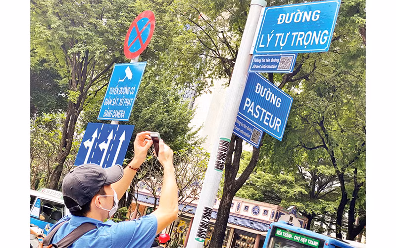 Một du khách tra cứu thông tin tên đường từ mã QR gắn ở giao lộ Lý Tự Trọng-Pasteur, quận 1.