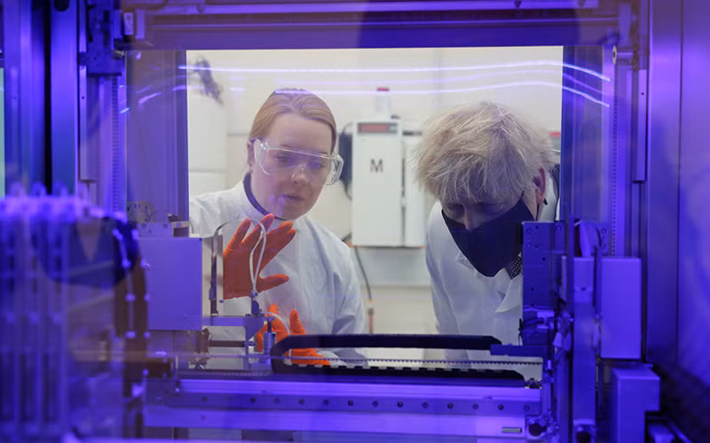 Thủ tướng Anh Boris Johnson (bên phải) đang quan sát máy xét nghiệm PCR (xét nghiệm virus SARS-CoV-2) cùng với nhà khoa học y sinh. Ảnh: AP.