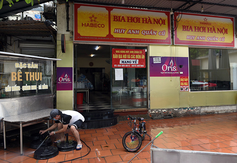 Nhân viên một quán bia trên phố Nguyễn Khánh Toàn (Cầu Giấy) tranh thủ vệ sinh cửa hàng, chuẩn bị bán hàng trở lại. “Vùng xanh” Hà Nội trong ngày đầu cơ sở kinh doanh mở cửa trở lại -0