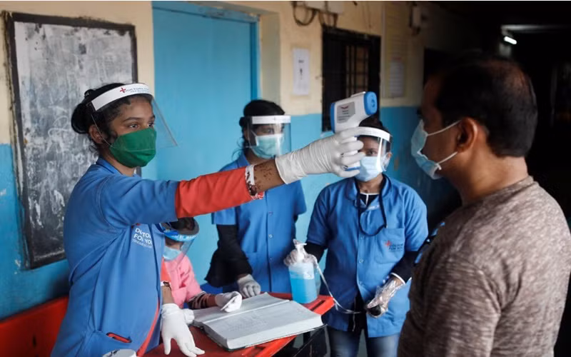 Nhân viên y tế đo thân nhiệt cho người dân tại một trường học ở Mumbai, Ấn Độ, ngày 10-8. (Ảnh: Reuters)