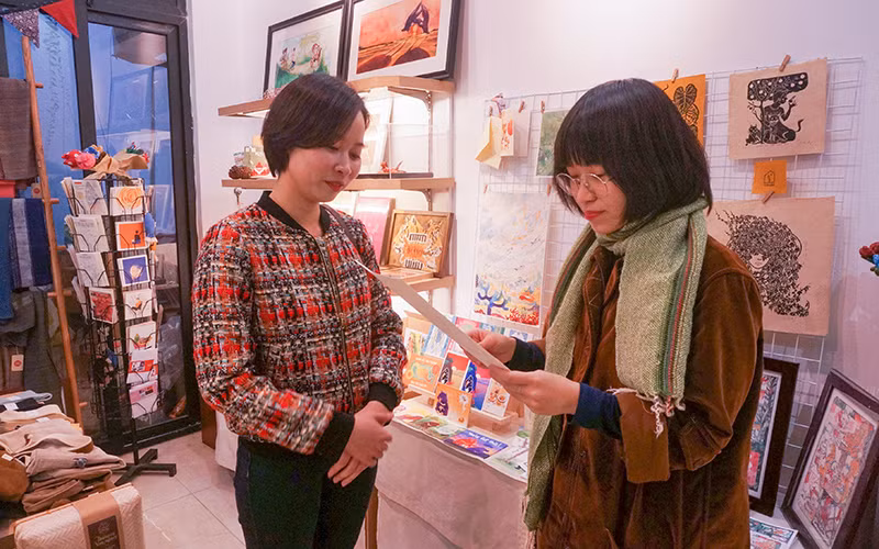 Ngô Thu Huyền (trái) giới thiệu sản phẩm bằng giấy dó.