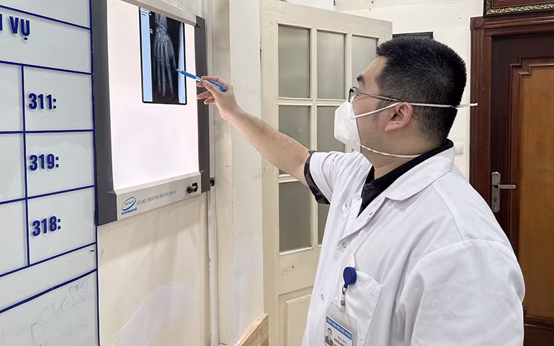 Bác sĩ Bệnh viện Hữu nghị Việt Ðức đánh giá tổn thương bàn tay của người bệnh vừa dùng điện thoại vừa sạc bị nổ. (Ảnh THẢO MY)