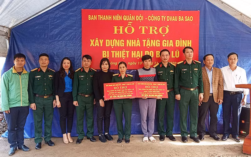 Sĩ quan dự bị Trần Hữu Diệu (áo xám trong ảnh) nhận nguồn hỗ trợ, động viên để xây dựng “Ngôi nhà 100 đồng” từ đại diện Ban Thanh niên quân đội ngay trên nền căn nhà cấp 4 vừa bị lũ cuốn trôi.