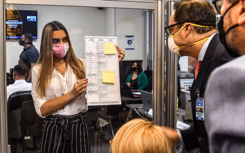 Các nhân viên bầu cử kiểm tra một lá phiếu được bầu qua đường bưu điện tại Miami, ngày 3-11-2020. (Ảnh: Getty Images)