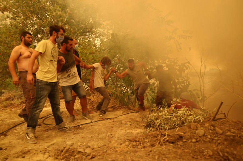 Người dân nắm tay nhau vượt qua đoạn dốc. (Ảnh: Reuters) Hàng nghìn người sơ tán khỏi đảo Evia (Hy Lạp) do cháy rừng -0