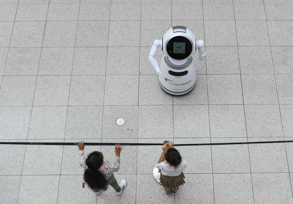 Em nhỏ lắng nghe robot thông minh giải thích các biện pháp phòng chống Covid-19 trong một trung tâm mua sắm tại TP Frankfurt, Đức. (Ảnh: Tân Hoa xã) 16.jpg -1