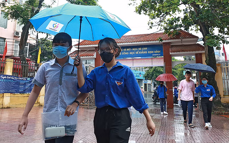 Các tình nguyện viên áo xanh che ô đưa từng thí sinh vào phòng thi tại điểm thi Trường Trung học phổ thông Nguyễn Khuyến (thành phố Nam Định).