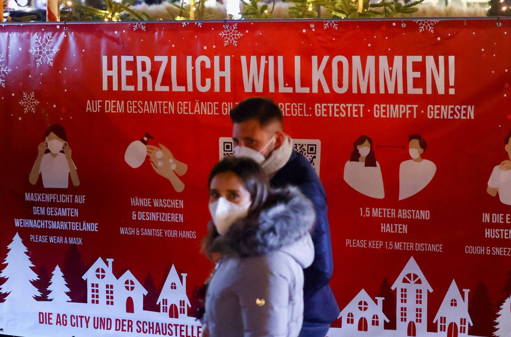 Một tấm biển chào mừng yêu cầu du khách đeo khẩu trang khi đến thăm 1 khu chợ Giáng sinh ở Berlin. Đức đã lên kế hoạch giảm quy mô các hoạt động tập trung đông người và tăng cường các biện pháp phòng dịch khác trong những ngày nghỉ lễ cuối năm. (Ảnh: Reuters) Châu Âu đón Giáng sinh trong lo ngại làn sóng Omicron -0