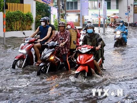 Người dân vất vả di chuyển trên đoạn ngập sâu ở đường Quốc Hương (thành phố Thủ Đức). (Ảnh: Hồng Giang/TTXVN)