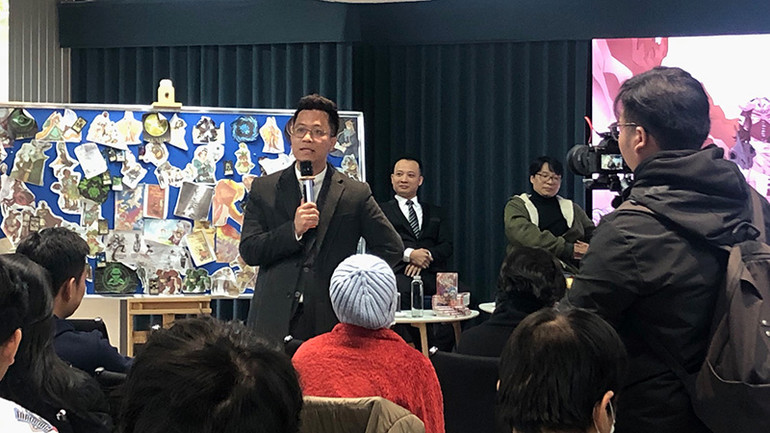 Bình luận viên Anh Quân chia sẻ với độc giả về bộ truyện, phía sau là tấm bảng của nhóm tác giả.