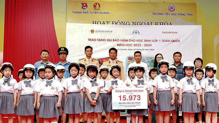 Đại diện các đơn vị trao tặng mũ bảo hiểm cho học sinh lớp 1 Trường tiểu học Hồng Thái. (Ảnh: LÝ THU)