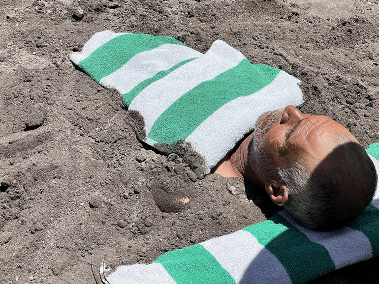 Một người đàn ông Ai Cập mắc bệnh vẩy nến vùi mình trong cát đen trên bãi biển Safaga ở Safaga, Ai Cập, ngày 5/5. (Ảnh: Tân Hoa Xã)