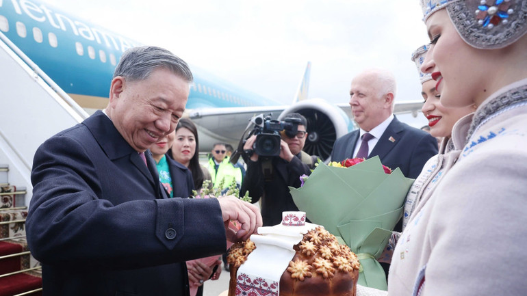 Thiếu nữ Belarus trong trang phục truyền thống trân trọng mời Tổng Bí thư Tô Lâm thưởng thức bánh mì và muối theo nghi thức đón khách quý của Belarus. (Ảnh: Thống Nhất/TTXVN)