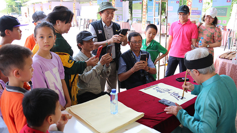Các em học sinh và người dân hai nước thích thú thưởng thức nghệ thuật thư pháp tại sự kiện. (Ảnh: Hải Tiến)