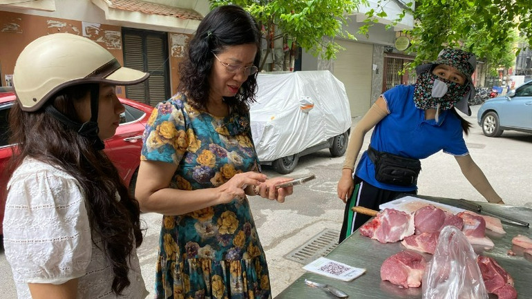 Người cao tuổi sử dụng điện thoại thanh toán không dùng tiền mặt khi đi chợ.