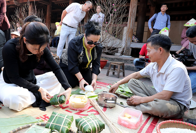 Du khách được nghệ nhân hướng dẫn cách gói bánh chưng.