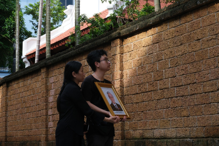 Hai mẹ con chị Lan cầm di ảnh hướng về ngôi nhà của Tổng Bí thư tại làng Lại Đà.