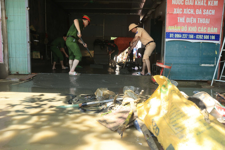 Cán bộ công an hỗ trợ người dân vệ sinh môi trường sau ngập lụt.