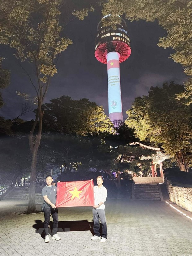 Hai thanh niên Việt Nam tại Hàn Quốc tự hào chụp ảnh bên lá quốc kỳ dưới chân tháp Namsan. (Ảnh: Đức Thắng/TTXVN)