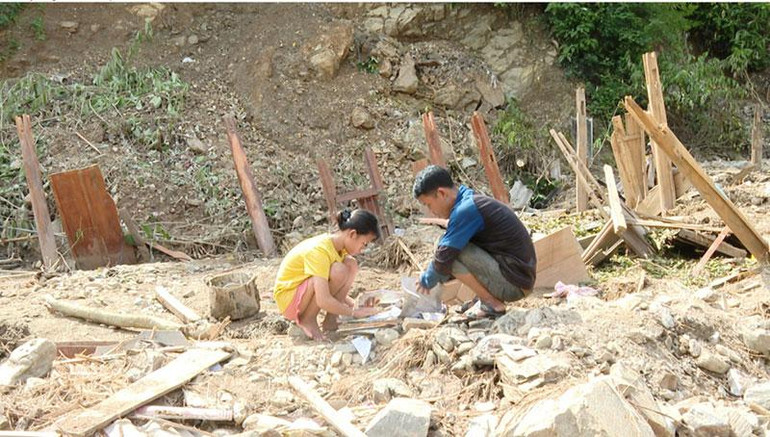Em Moong Thị Phương Thảo và bố nhặt lại những cuốn sách còn có thể dùng được trong ngôi nhà bị lũ cuốn trôi.
