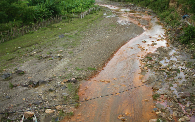Dòng nước vàng sẫm và bùn chảy từ khu vực đỉnh núi, nơi có hoạt động khai thác khoáng sản nhập vào suối Nậm Huống.