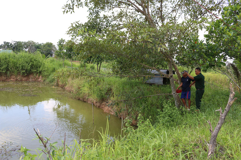 Đại úy Trần Mạnh Tiến, cán bộ Đồn Biên phòng cửa khẩu Đắk Ruê cùng ông Phạm Văn Mến tới kiểm tra ao cá của gia đình. (Ảnh: BÍCH NGUYÊN)